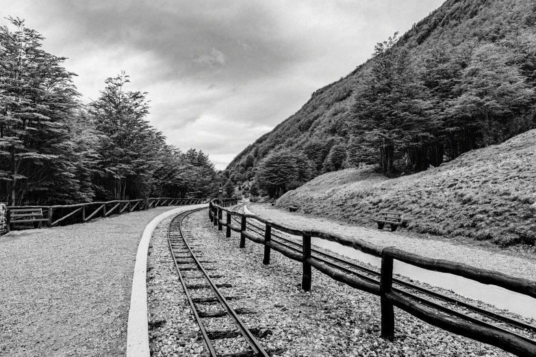 a train track running down a road with trees and hills in the background