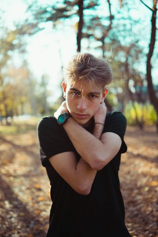 a man standing in front of trees while holding his head to his side