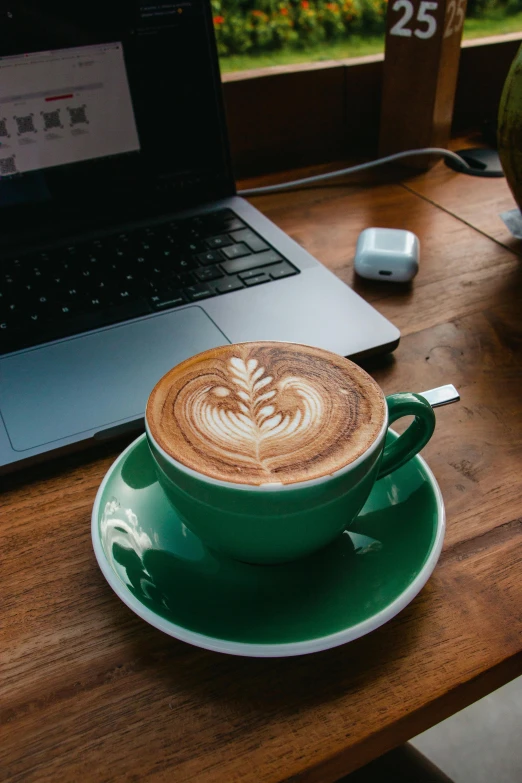 a cappuccino in a green saucer next to a laptop