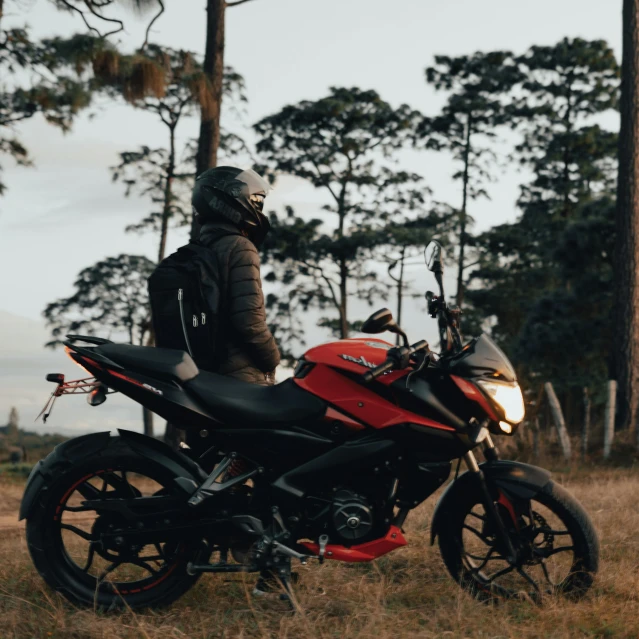 a person standing next to a parked red motorcycle in a field