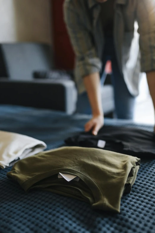 a woman unrolls an olive green colored shirt from the bed