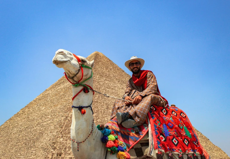 a camel in front of a pyramid with a person riding on top