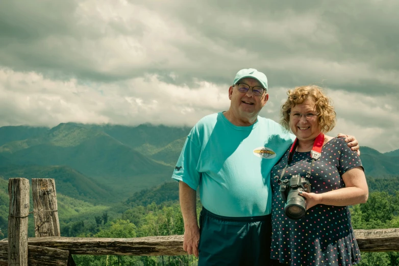 a couple standing on top of a mountain next to a fence