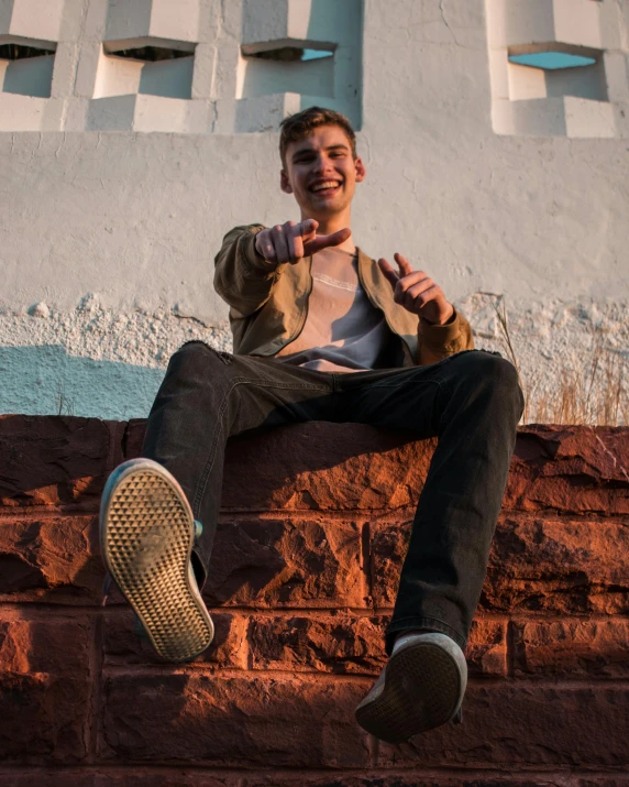 a young man sitting on a brick wall making the finger sign