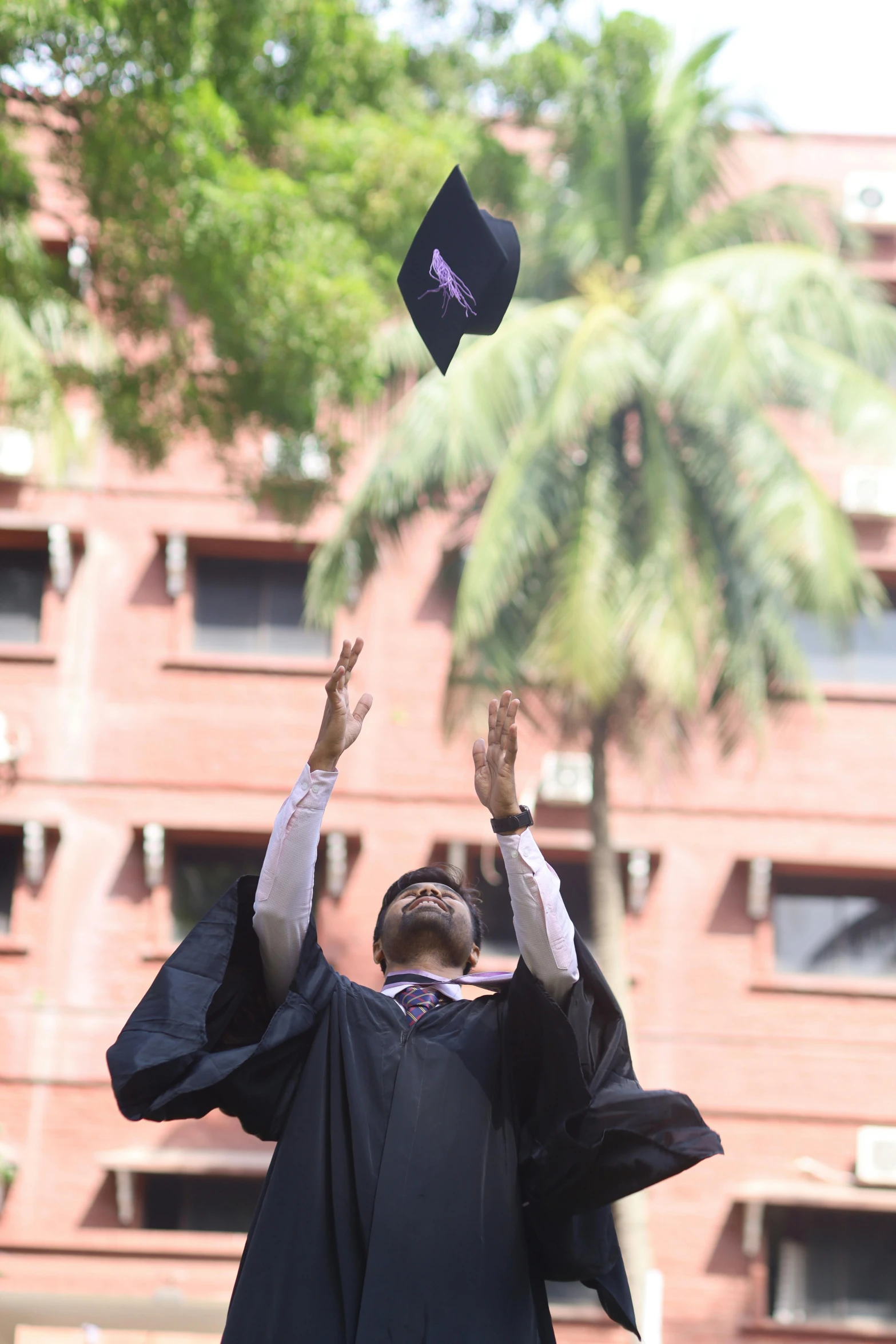 a man wearing a black graduation gown tossing a hat