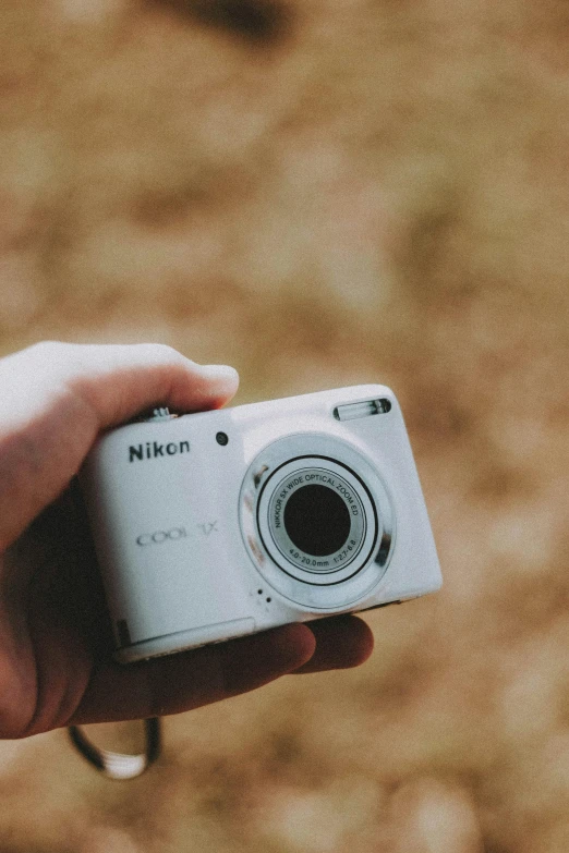 hand holding white camera up against a brown wall