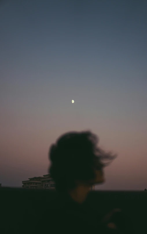 a boy looking over the horizon with his head covered in a messy ponytail