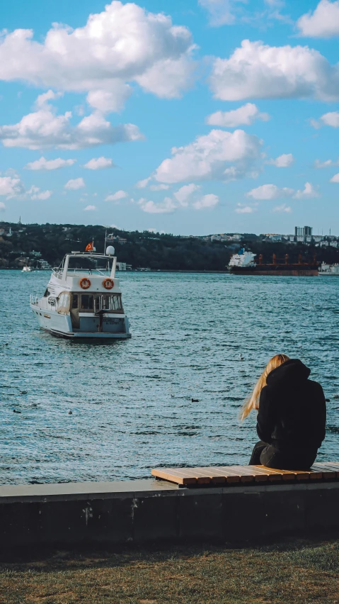 a man sits watching a boat in the water