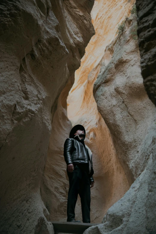 man in jacket standing next to rock wall with a narrow passage