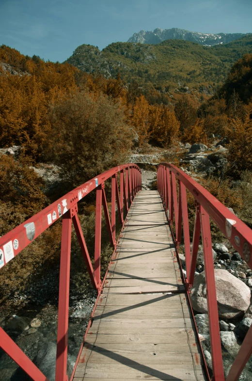 a red bridge crosses over some rocks near a hill