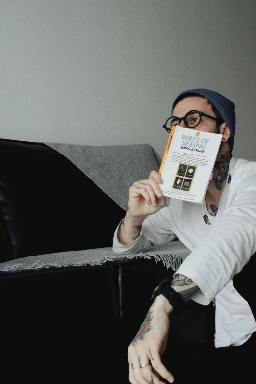 a man with black glasses and a beard sitting on a couch holding up an object