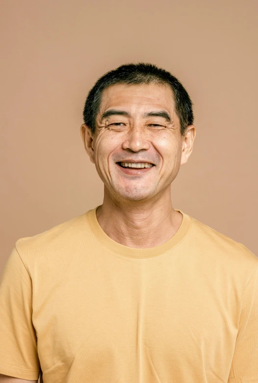 an asian man wearing a tan shirt smiling