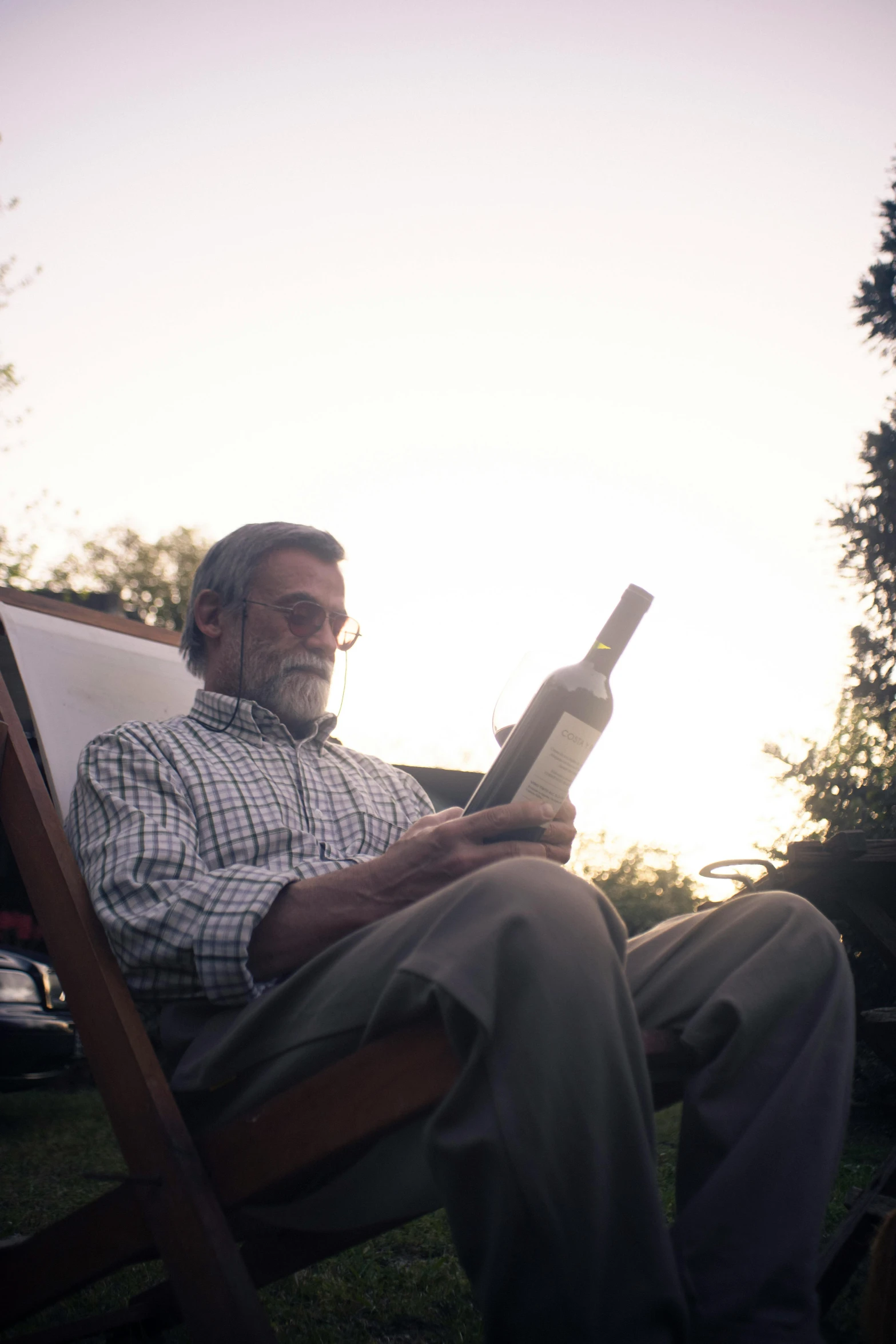 man sitting in chair holding up wine bottle