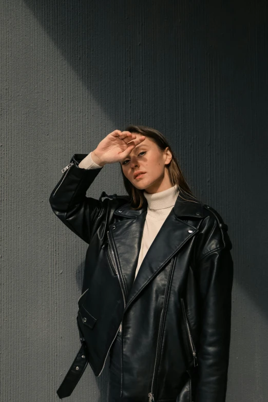 a woman wearing a black jacket is holding her hands behind her head