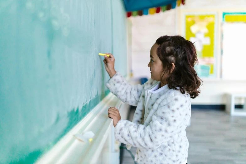 a little girl writing on the wall next to a chalk board