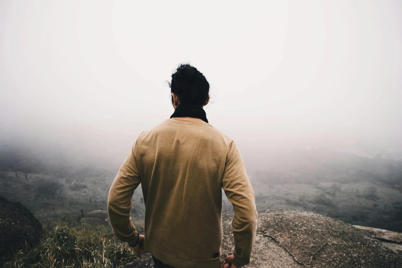 the man is standing on top of the mountain looking at the fog