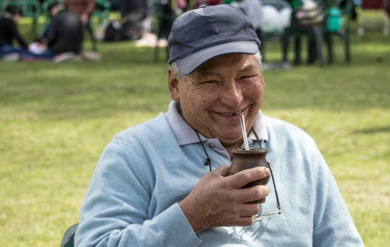 an old man smiles while he drinks a beverage