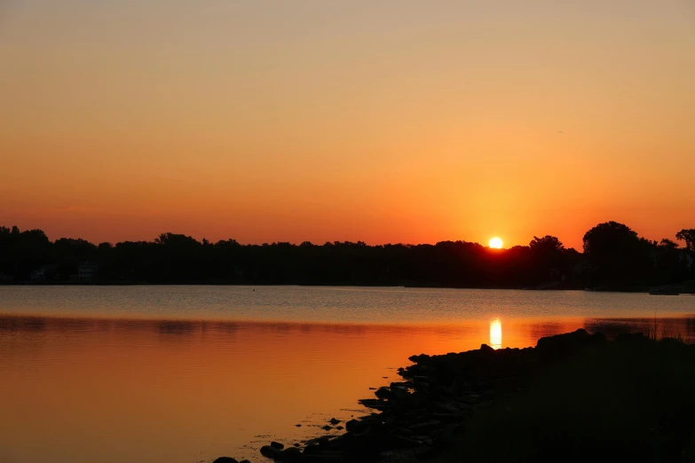 the sun is setting over the water on the shore