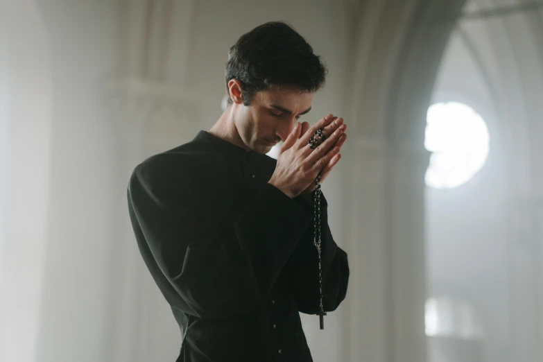 a man wearing black standing in front of a mirror praying