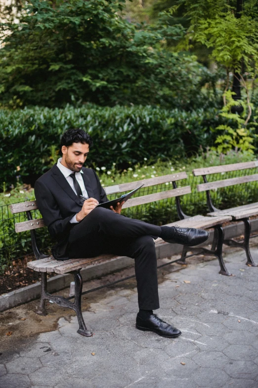 a man in a suit is sitting on a bench and texting