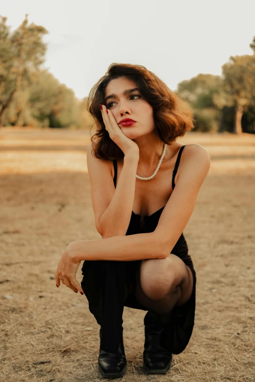 a woman with a bare  and a necklace on, crouching against the ground