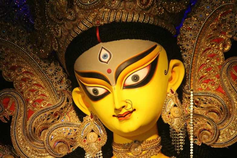 a yellow painted indian doll with many eyes