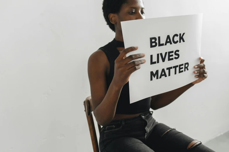 an african american girl is sitting down holding a white sign that says, black lives matter