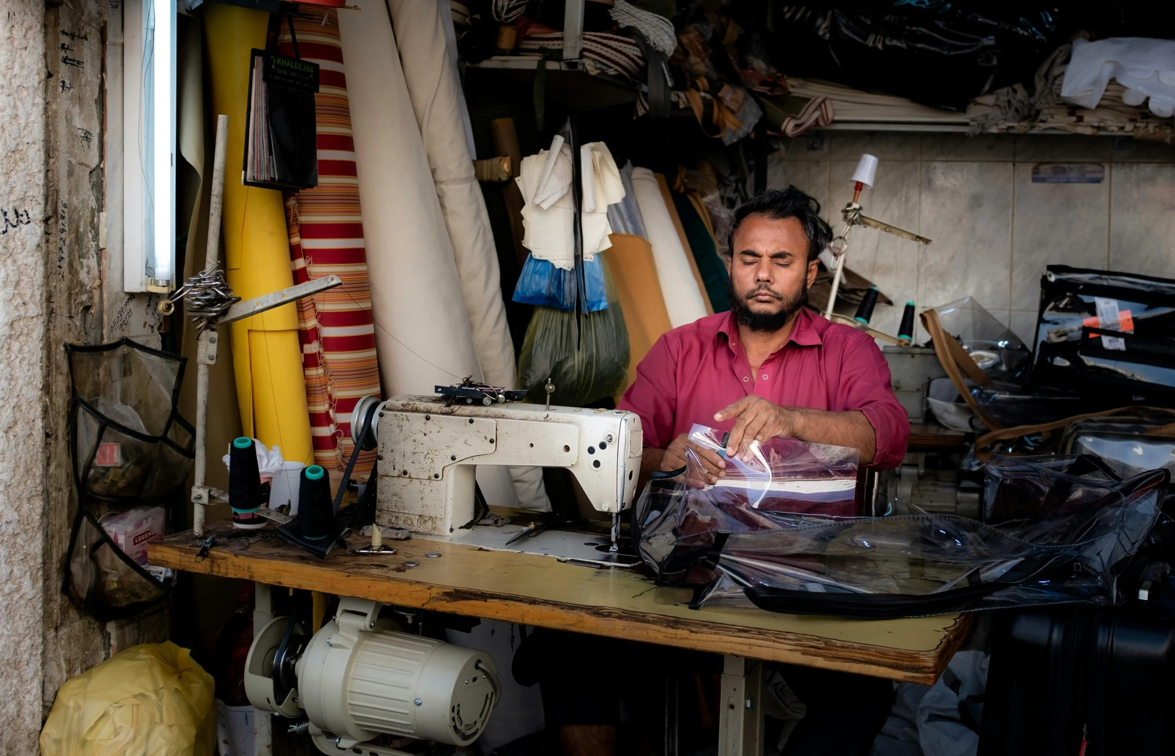 a man in a pink shirt is sitting in his shop making clothes