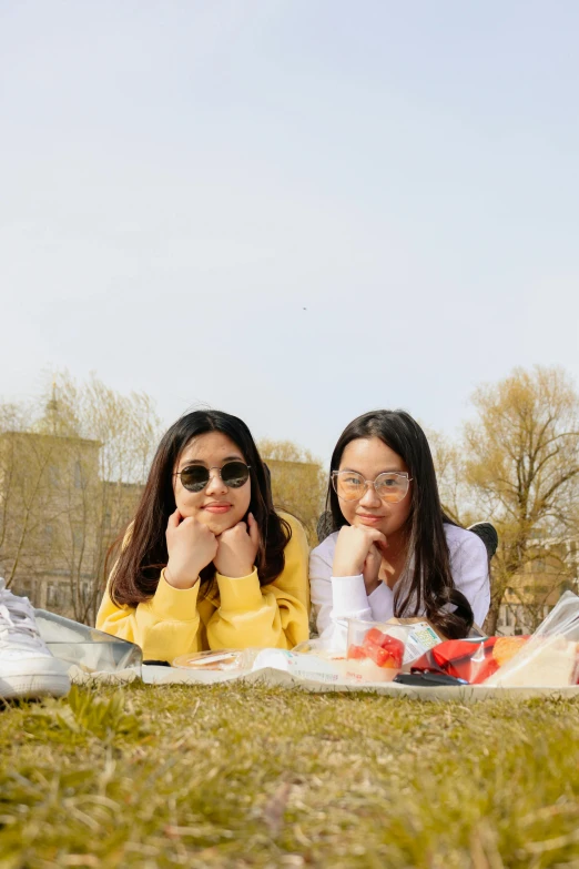 two girls in sunglasses sitting on the ground together