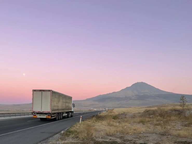 a large truck driving down a highway with a mountain in the background