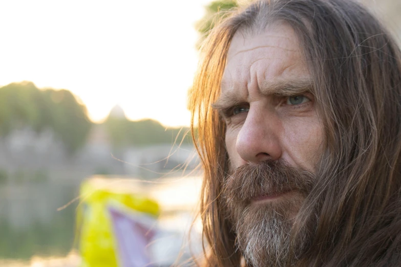 a bearded man with long hair looks off into the distance