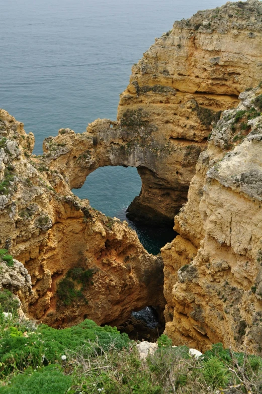 an old arch made of rocks on the ocean near the beach