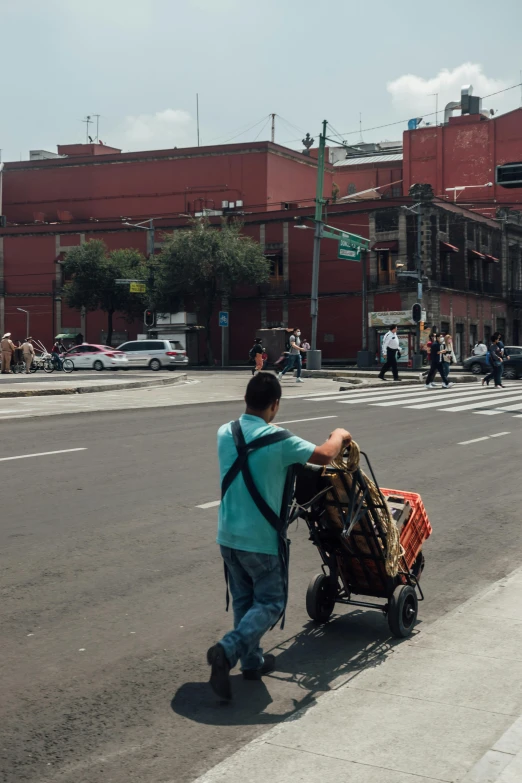 a young person hing a cart filled with luggage across a city street