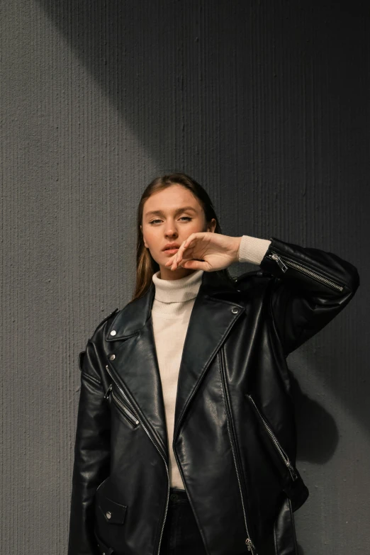 woman in black jacket leaning up against wall with hand on hip