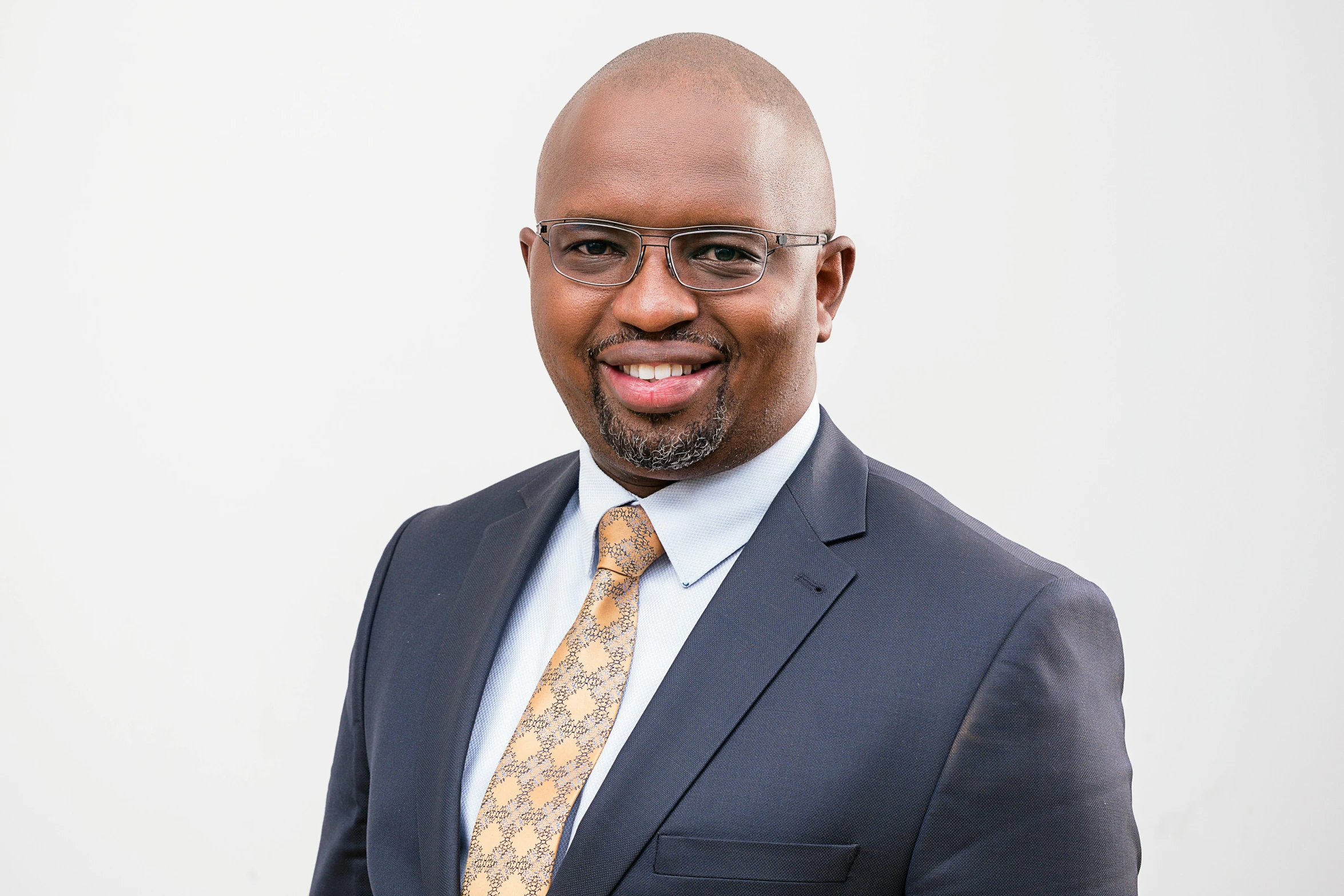 a bald man wearing glasses and a suit smiles in front of the camera