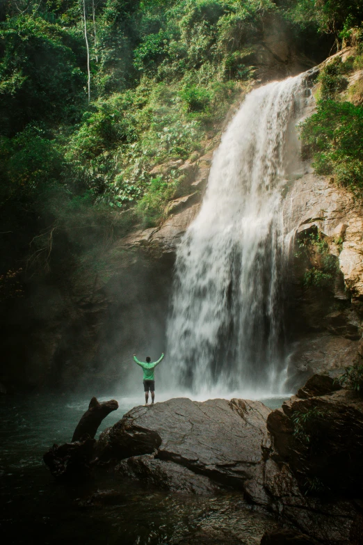 man standing on a rock at bottom of a waterfall