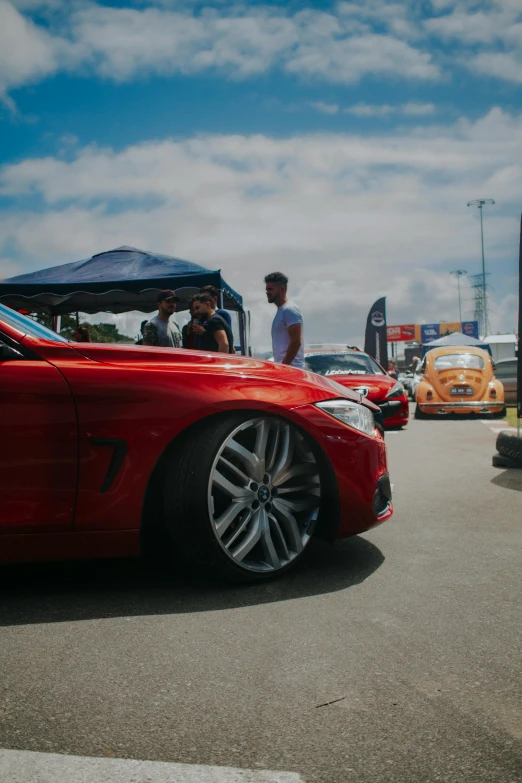 people are standing on a platform looking over a red sports car