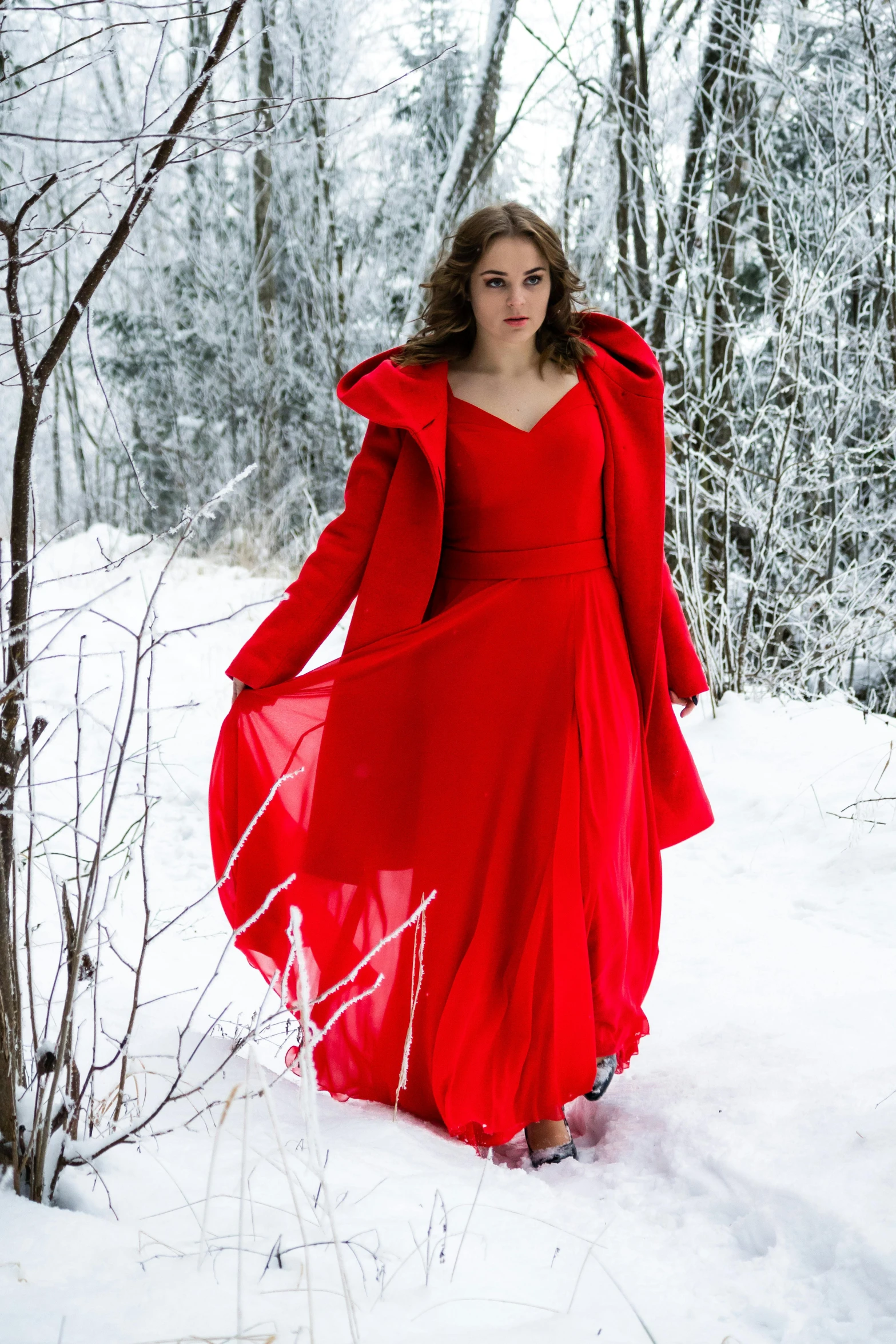 the woman in a red dress stands in the snow