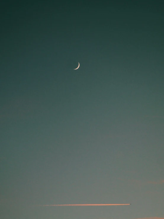 the moon, a contrail, and a plane in the distance