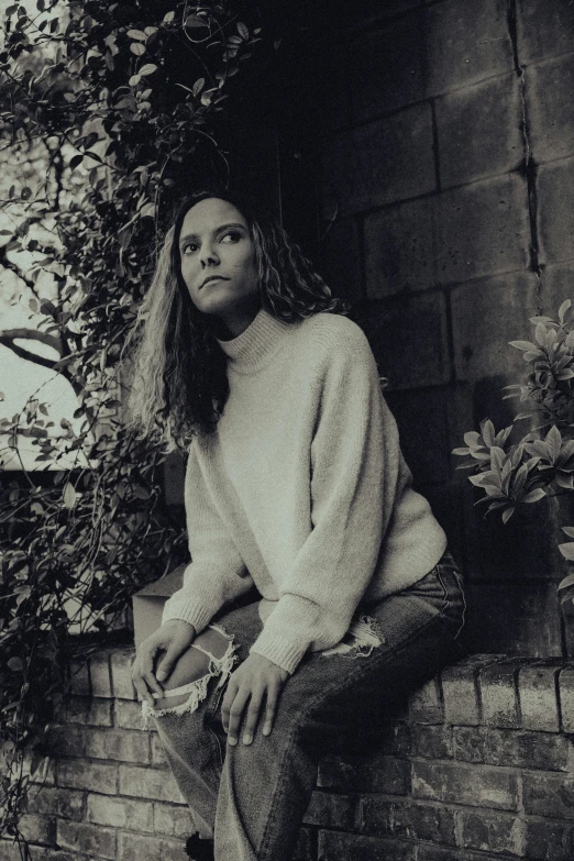 a woman is leaning against a wall while wearing a sweater