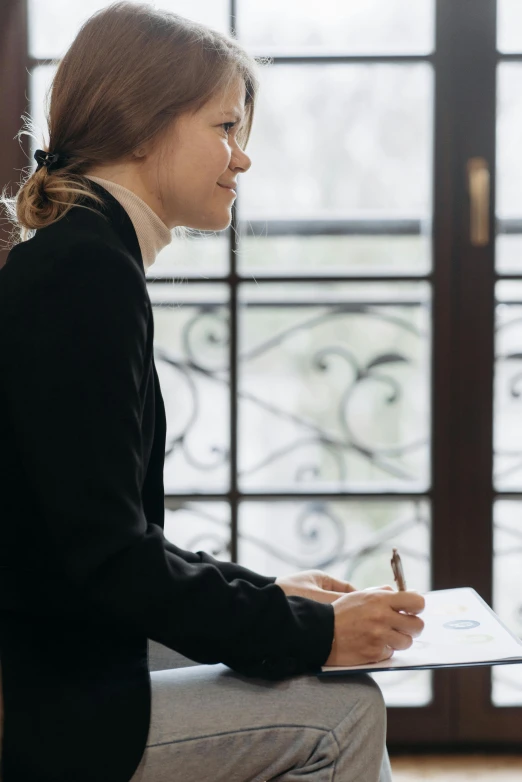 a woman is sitting on a stool and writing soing