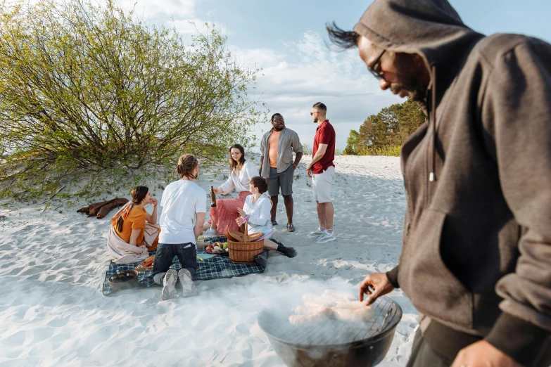 a group of people stand around a picnic spread on the sand