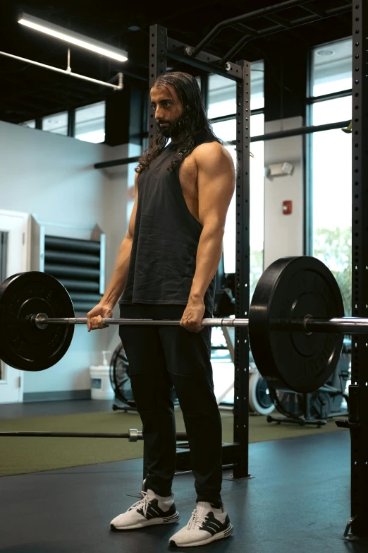 a man with long hair and a beard standing in front of a barbell