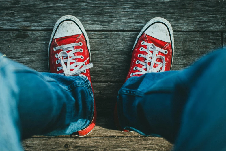 pair of red sneakers and blue jeans standing on a wood floor