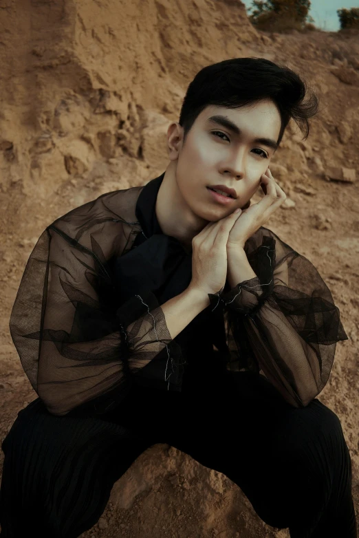 young man sitting down on a rock wearing a shirt and black pants