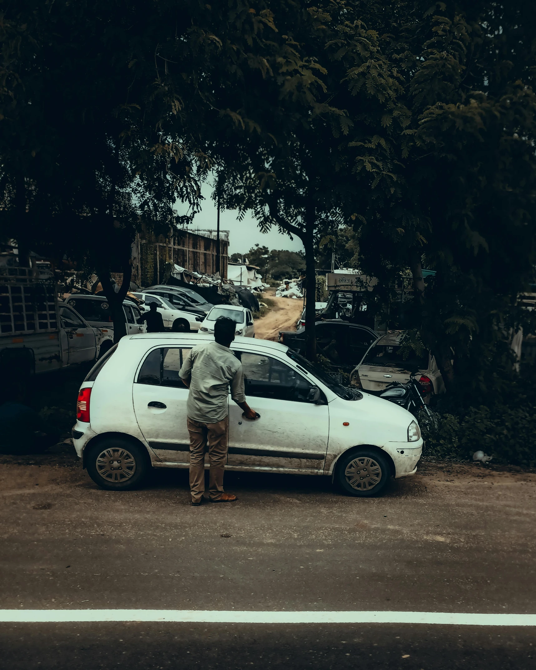 a man standing near a white car by some trees