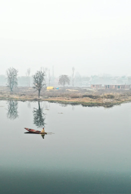 a lone canoe is floating on a lake on a foggy morning