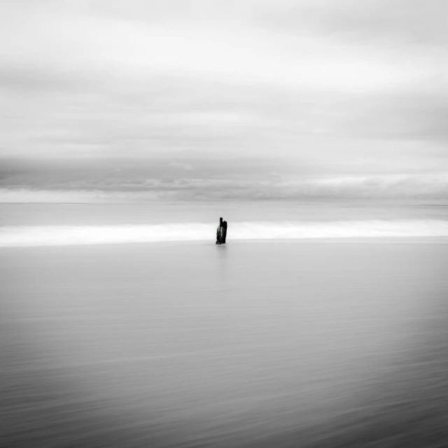 lone man standing on the edge of a body of water with dark clouds overhead