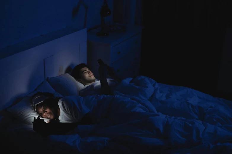 two people in a bed with blue sheets in the dark