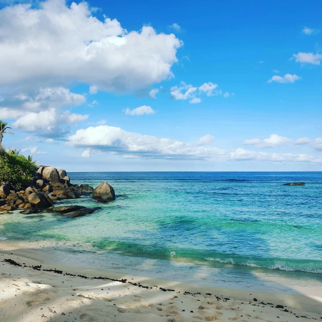 a sandy beach with bright blue water and a green hillside